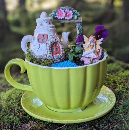 a green teacup with a miniature fairy garden inside
